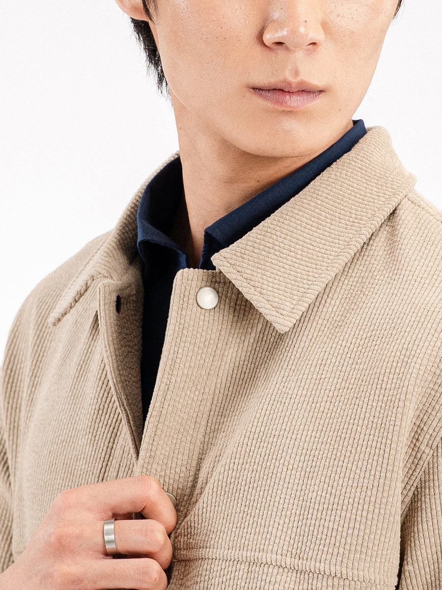Man wearing beige corduroy jacket over navy shirt, stylish men's apparel