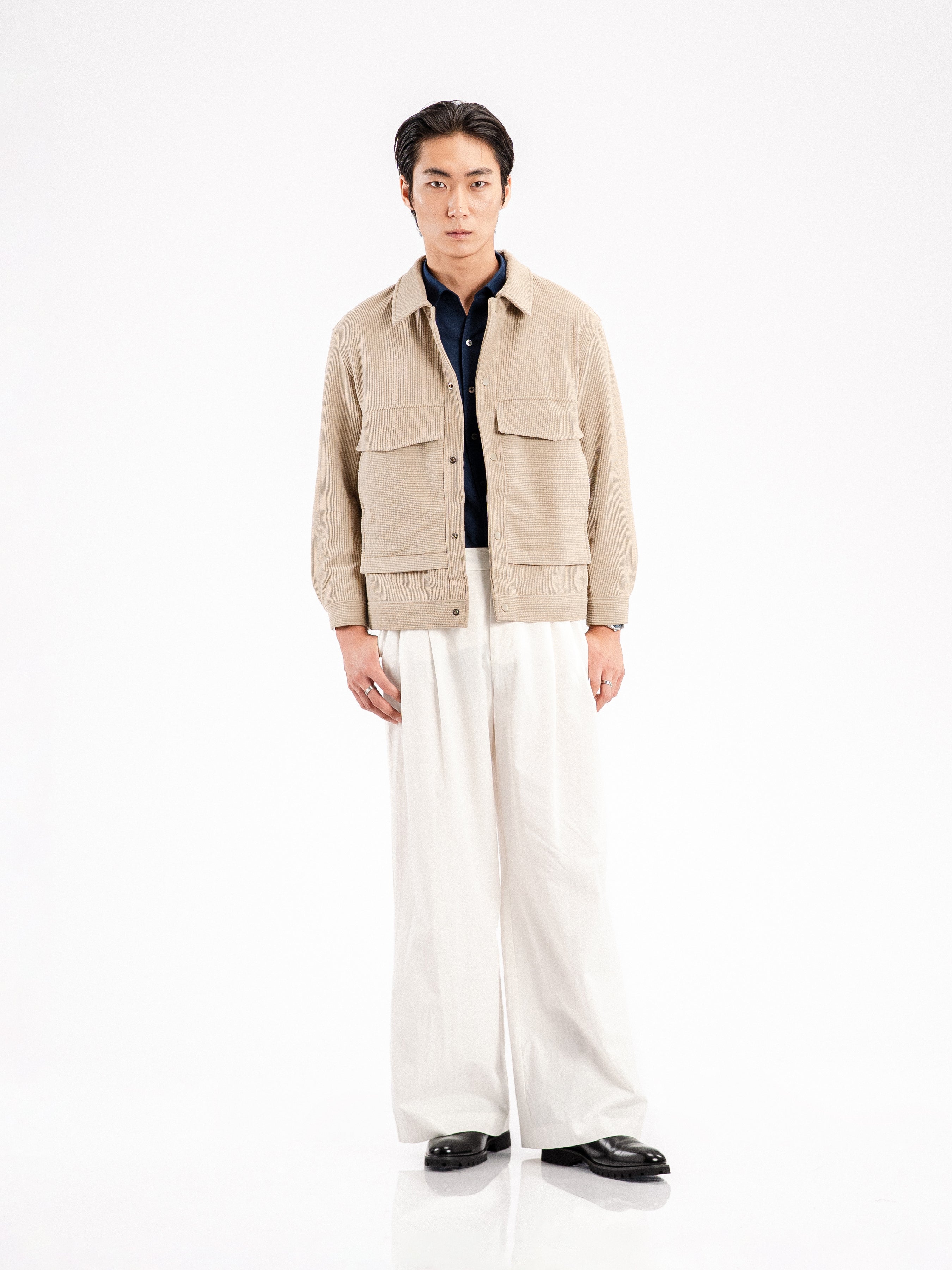 Men's beige corduroy jacket with navy shirt, white wide-leg pants, and black formal shoes
