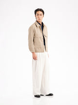 Men's beige corduroy jacket with navy shirt, white wide-leg pants, and black loafers for stylish casual wear