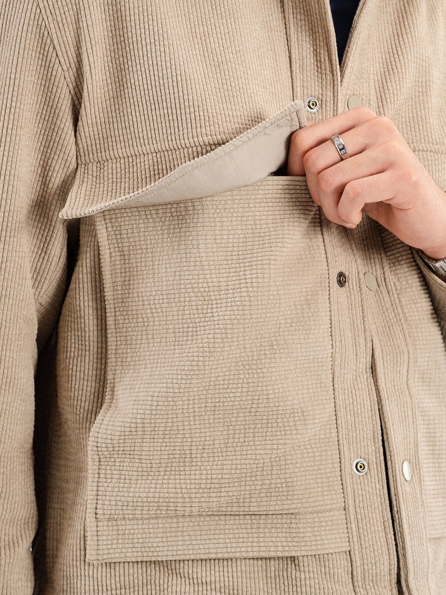 Beige corduroy jacket with front pocket, button closure, and man's hand wearing ring