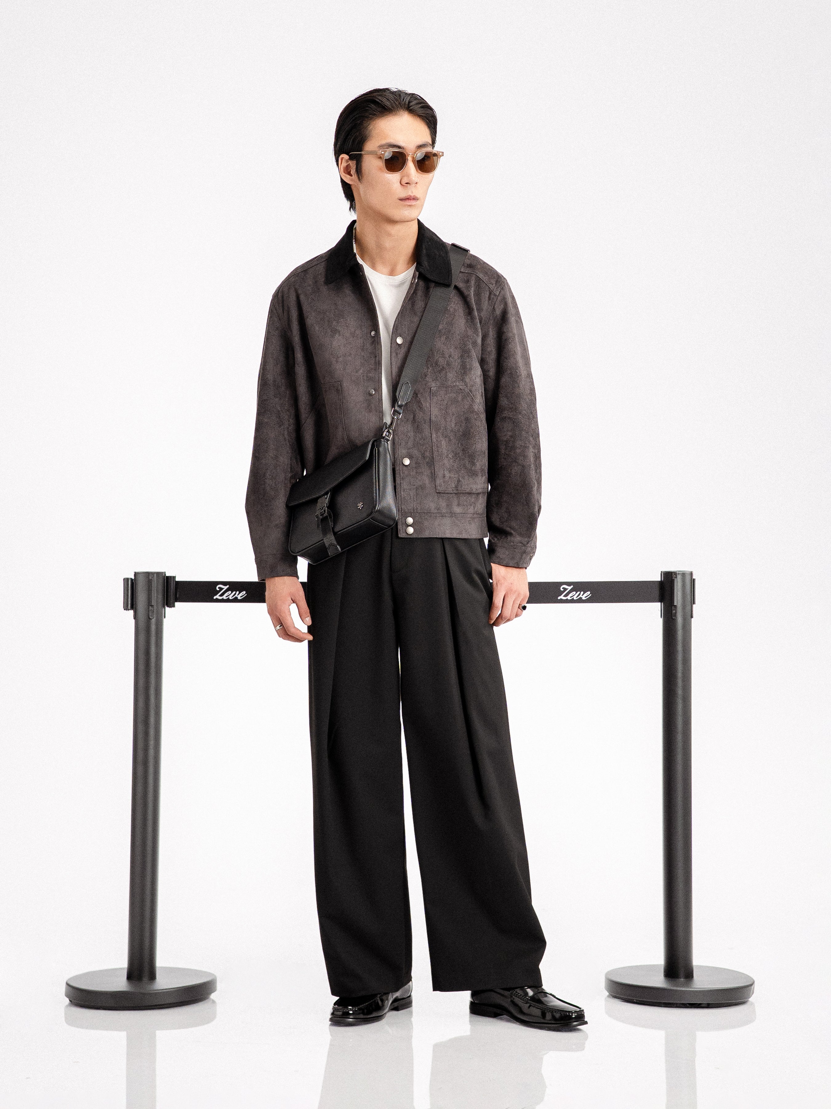 Man in stylish men's apparel: suede jacket, wide-leg trousers, loafers, and crossbody bag