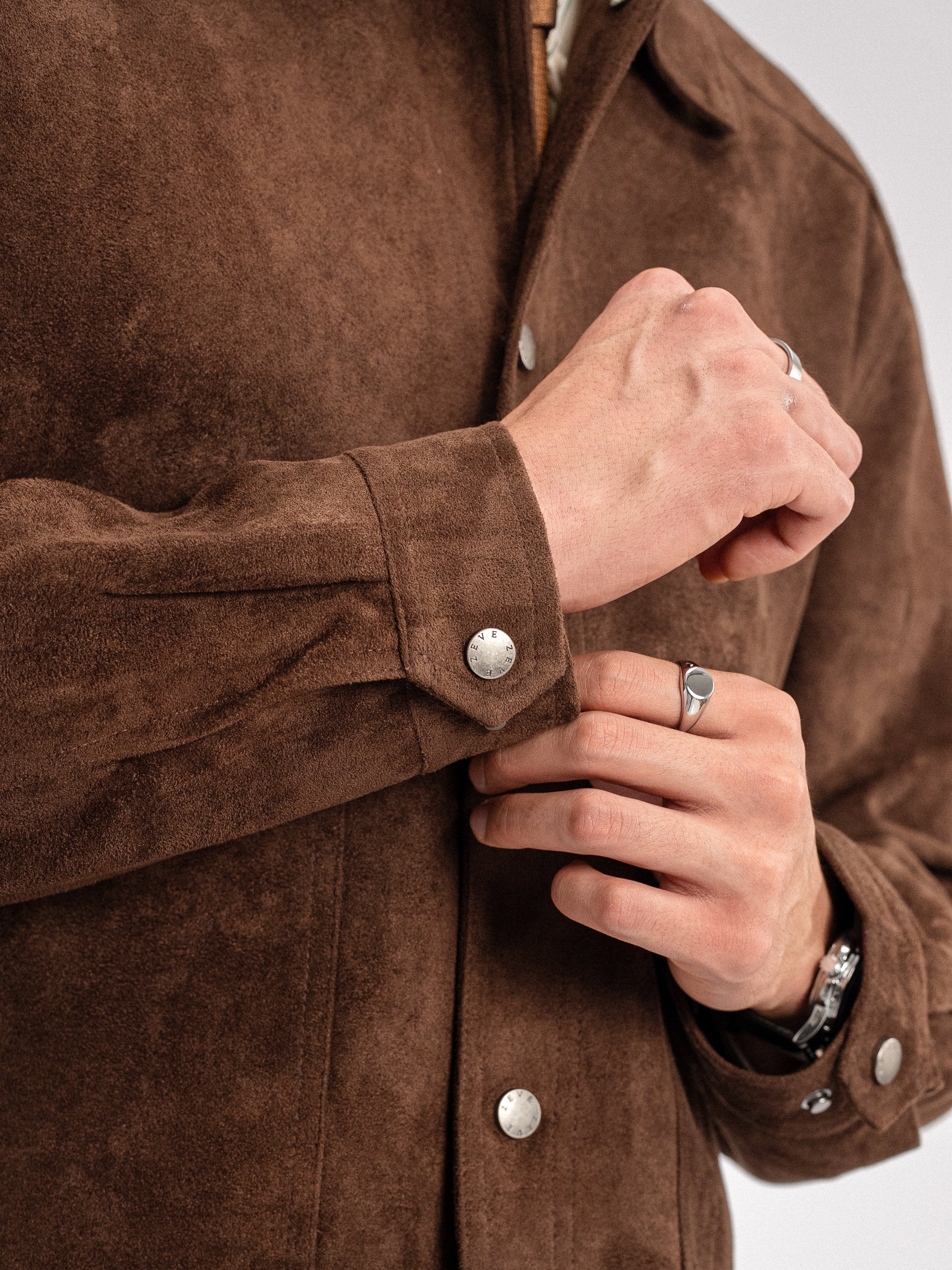 Brown suede men's jacket with silver buttons, styled with rings and watch for smart casual look