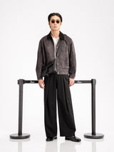 Man in stylish black loafers, wide-leg pants, and suede jacket with crossbody bag, sunglasses, minimalist studio setting