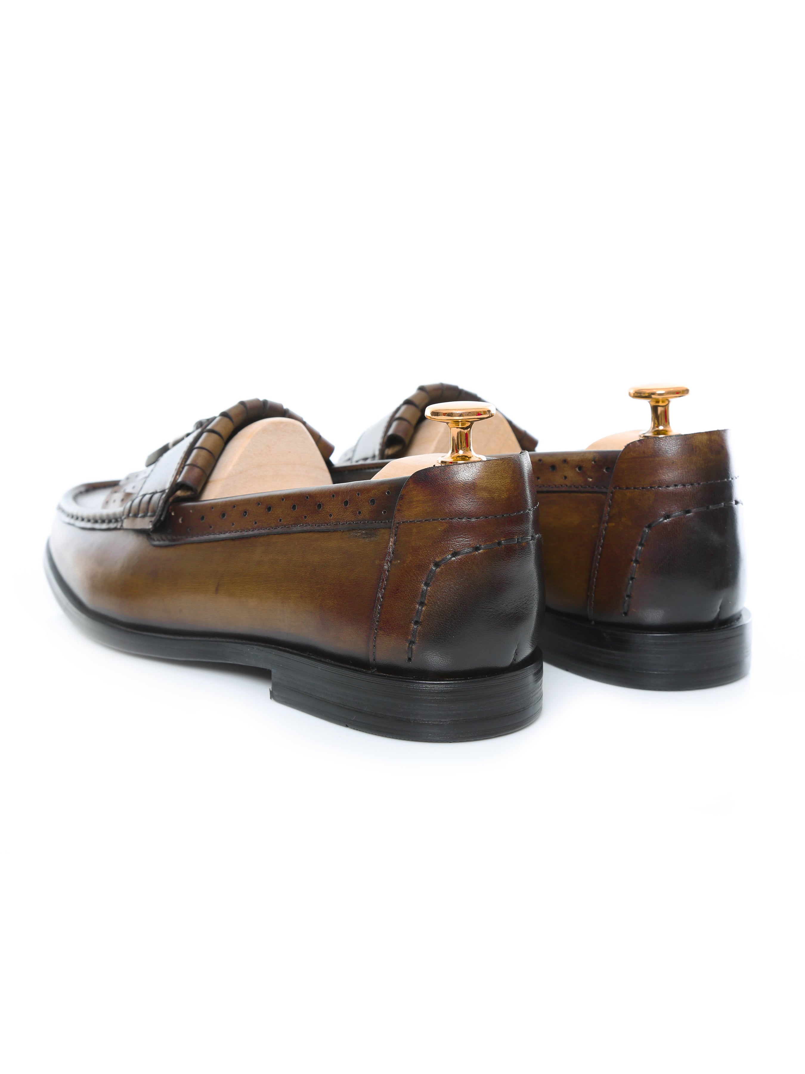 Handmade brown leather men’s loafers with fringe detail and patina finish on white background